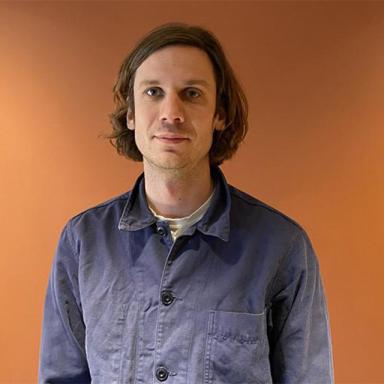 man visible from waist up standing in front of an orange background